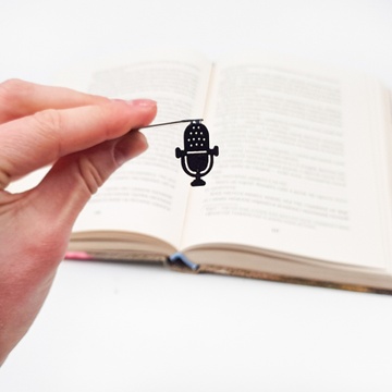 Black metal bookmark Microphone. A falt metal stick stays between the pages of the book. The silhouette of the microphone is on the side of the book. It is visible even when the book is closed.